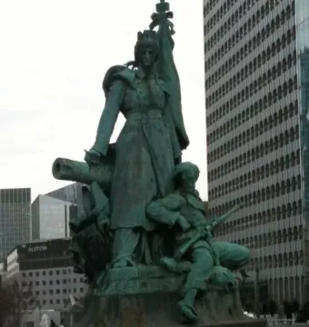 La Défense de Paris bronze monument with a crowned female figure, standard, cannon, and seated soldier in front of modern buildings
