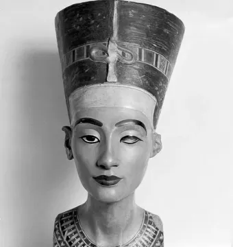 Bust of Nefertiti with a tall striped crown and decorated collar, shown in black and white.