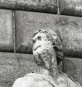 Pasquino, a severely weathered stone statue with a missing left arm, shown against rough stone blocks.