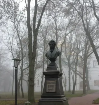 Bronze bust of Pushkin on a dark pedestal in a misty park.