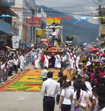 A religious procession float with San Juan Patrón and a crucified figure surrounded by flowers.