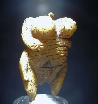 Venus of Hohle Fels figurine with a loop at the top, lit against a dark background