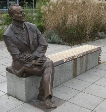 Willy Brandt Memorial bronze statue of a seated man in a suit on a bench, with tall dry grasses behind it.