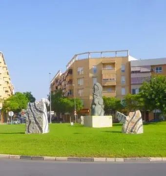 Dona Lluna sculpture with a crescent moon on its head standing on a pedestal in a grassy roundabout