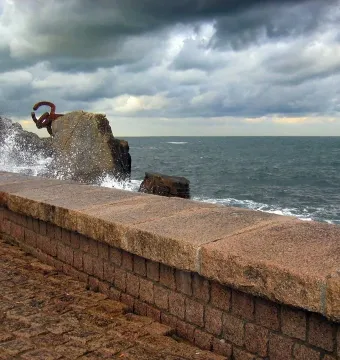 Peine del Viento sculpture beside rocky cliffs as a wave crashes into the rust-colored metal forms.