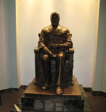 Timothy Eaton statue seated on a dark tiered pedestal in an alcove under spotlights.