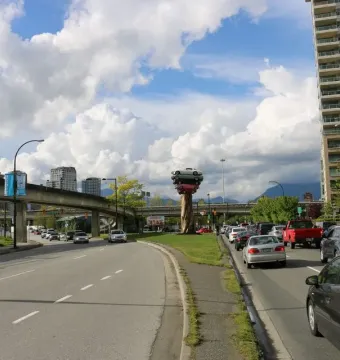 Trans Am Rapture sculpture made of stacked cars on a tree-trunk-like base beside busy roads in Vancouver.