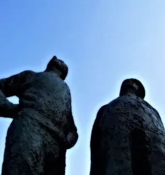Two Working Men sculpture seen from below against a clear blue sky.