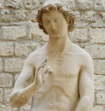 Adam stone sculpture with a raised left hand and fig leaves covering the lower body
