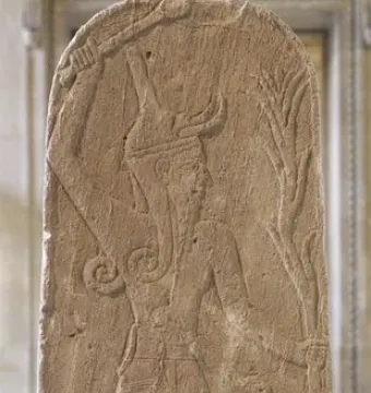 Baal with Thunderbolt carved on a weathered stone stele, shown with a horned figure holding a club and a stylized plant-like shaft beside a smaller figure.