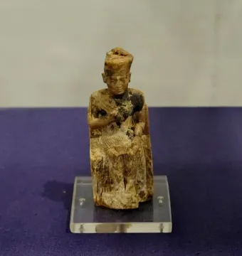 Khufu statuette of a seated figure wearing a tall crown and holding an object in its lap.