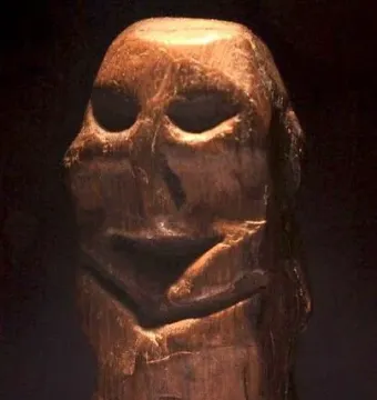 Mannetje van Willemstad wooden statuette with deep eye hollows and a recessed mouth on a transparent base.