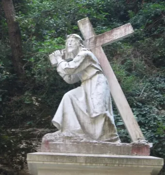 Monumental Rosary of Montserrat sculpture of Jesus carrying a cross beside dense greenery