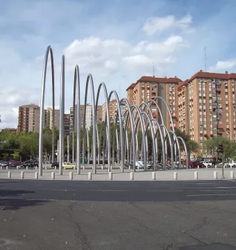 Puerta de la Ilustración sculpture with shiny silver arch-like forms on a traffic island in Madrid.