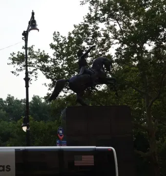 Simón Bolívar Equestrian Statue on a rearing horse, seen as a bronze silhouette against the sky and trees.