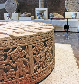 Stone of Motecuhzoma I, a large round stone monolith with carved figures and symbolic reliefs displayed in a museum setting.