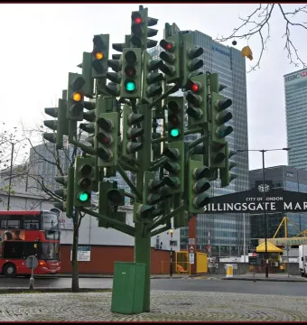 The Traffic Light Tree sculpture made from green traffic light poles, with illuminated red, amber, and green signals in an urban street setting.