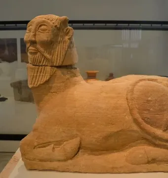 The Bicha of Balazote stone sculpture displayed on a museum plinth, with glass display cases in the background.