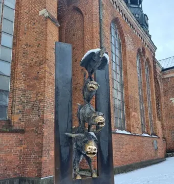 Bremer Stadtmusikanten bronze sculpture of a donkey, dog, cat, and rooster stacked in a metal frame beside a brick building.