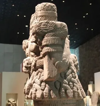 Coatlicue stone sculpture with serpent motifs, skull-like necklace details, and a textured skirt.