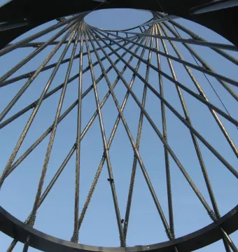 Upward view through Mae West’s metal ring and lattice of converging rods against a blue sky.