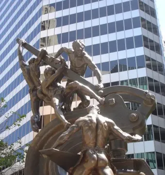 Mechanics Monument showing a dark metal sculpture of muscular workers operating machinery in front of an office building