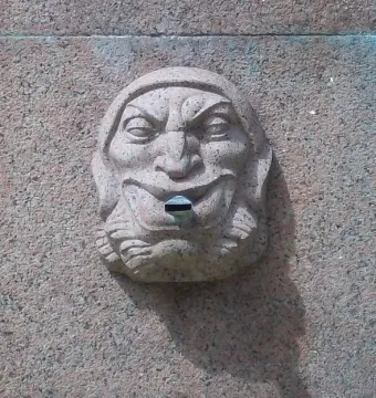 Carved stone face with a wide smile and metal spout on the Obelisk of Montevideo.