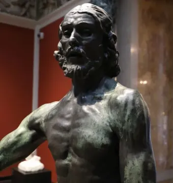 Bronze bust of Saint John the Baptist with long hair and a beard, showing a dark greenish patina.