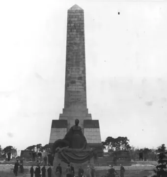 The Soviet War Memorial Schönholzer Heide with a tall stone obelisk and seated statue, surrounded by people on the steps.