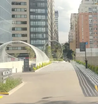 The Eye of Mexico sculpture frames an urban pathway between modern high-rise buildings and landscaped greenery.