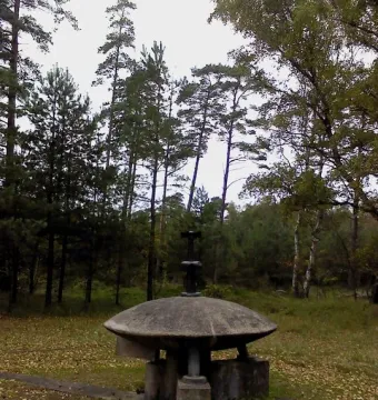 UFO Memorial concrete sculpture in a forest setting with a flat top and pipe-like fixture.