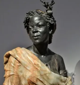 Bust of Woman from the French Colonies with tightly curled hair and a floral headpiece on a pedestal.