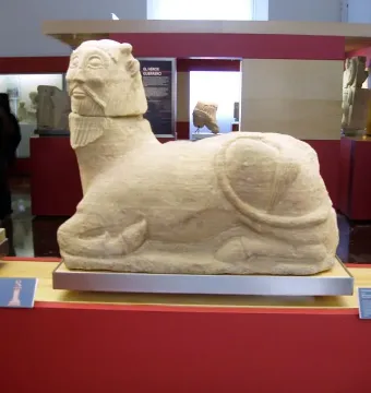 Bicha of Balazote stone sculpture with a bearded human head and animal body on display in a museum
