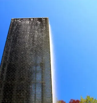 Crown Fountain tower with water cascading down its dark brick-like surface against a blue sky.