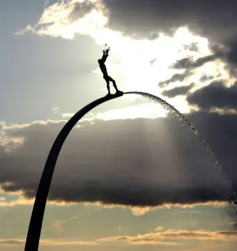 Silhouetted figure atop the God, Our Father on the Rainbow fountain with water cascading down the arch.