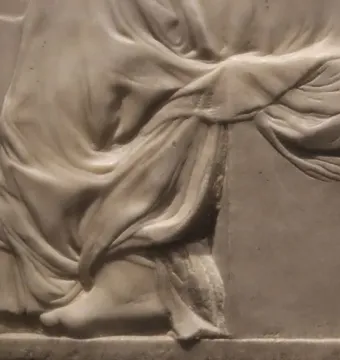 Close-up of Madonna of the Stair showing the lower half of the relief, with draped fabric, bare feet, and stair-like lines in the background.