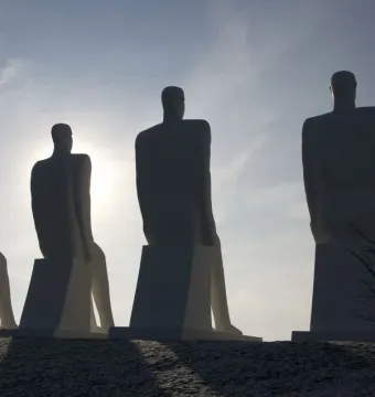 The Man by the Sea sculpture seen from behind as four seated figures silhouette against a bright sky.