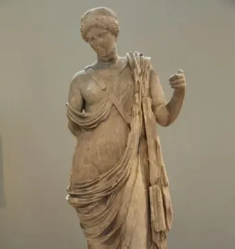 Marble statue of Armed Aphrodite standing in flowing drapery with her head bowed, showing wear and damage.