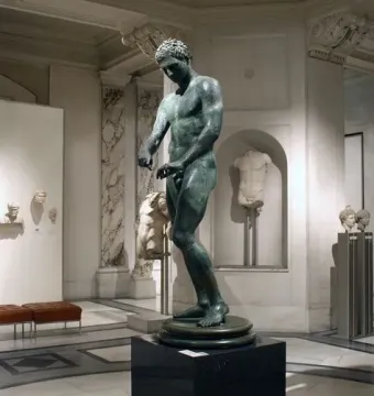 Bronze statue of the Athlete from Ephesus on a pedestal in a museum gallery.