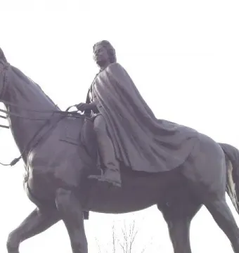 Low-angle view of the Elizabeth II equestrian statue showing a cloaked rider on a saddled horse against the sky.