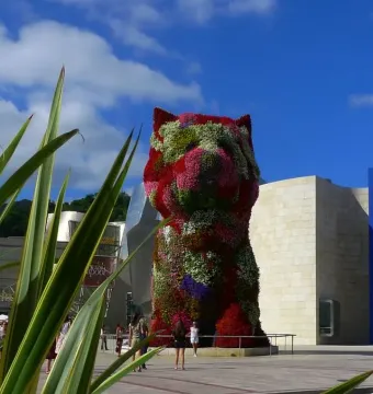 Puppy floral dog sculpture covered in red, pink, white, and green flowers in an outdoor plaza.