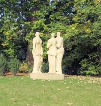 Three Standing Figures by Henry Moore stands on a grassy lawn with trees behind it.