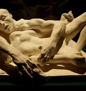 Avarice and Lust by Auguste Rodin, a cream-colored sculpture of two intertwined nude figures against a dark background.