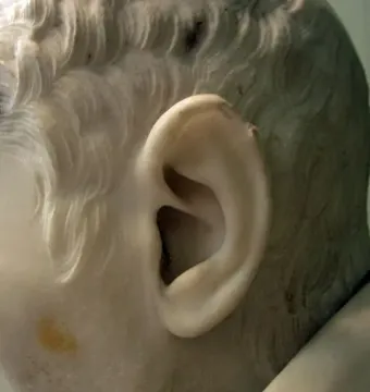 Close-up of Cardinal Alessandro Peretti’s marble ear and wavy hair with a faint yellow stain on the stone.