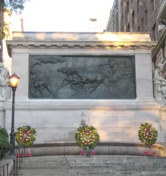 Firemen\'s Memorial with a stone relief of horses pulling a wagon, flanked by statues and wreaths.