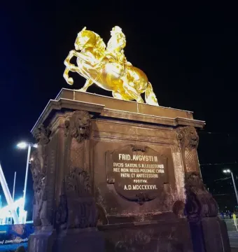 The Golden Rider equestrian statue glows against the night sky on a tall stone pedestal.