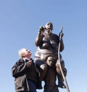 Survival of the Fattest bronze sculpture of a corpulent woman on an emaciated man, with a man standing nearby.