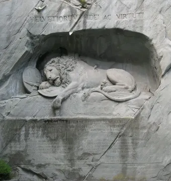 The Lion Monument in Luzern showing a wounded lion carved into a rock grotto with a shield and broken spear.