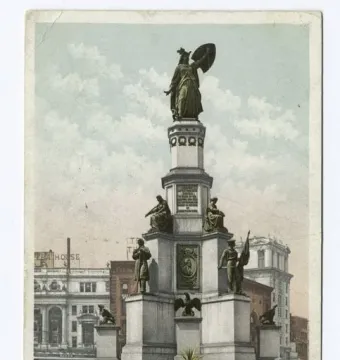 Michigan Soldiers\' and Sailors\' Monument rising in front of downtown Detroit buildings, with a pedestrian on the sidewalk.