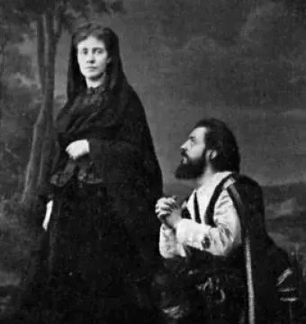 A woman in a dark flowing gown and veil stands beside a kneeling bearded man with clasped hands in The Stone Guest.